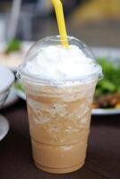 Ice latte shake coffee with whipped cream in plastic glass and meal food on wooden table in cafe and restaurant photo