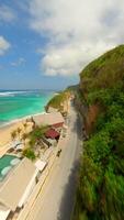 Cinematic FPV drone flight along Pandawa Beach in Bali, showcasing turquoise sea, golden sand, beachfront resort, and coastal road carved into limestone cliffs. video