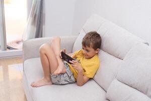 Child plays with mobile phone while slouching on the sofa, showing poor posture habits photo