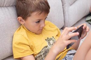 Child engaged with mobile device while sitting on a couch, exhibiting poor posture and a curved back photo