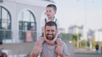 Father and son share joyful moments at a city park, with the child sitting on the father's shoulders, both smiling under the bright sun, surrounded by greenery. photo
