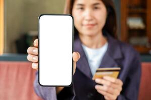 Close-up of a woman displaying a smartphone with a blank screen and holding a credit card, ideal for online shopping themes. photo