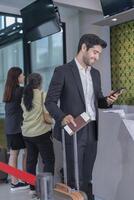 smiling businessman in suit one hand suit carry the suitcase and holding passport,other hand using smartphone,passengers getting service in the airport photo