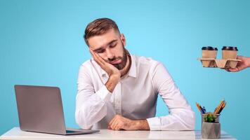 Handsome businessman tired of computer work sleeping at his desk on blue studio background, panorama. Exhausted male employee needing coffee, suffering from overwork after laptop use photo