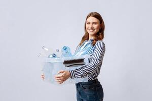 Waste Sorting Concept. Portrait Of Smiling Young Lady Carrying Container With Empty Plastic Bottles For Recycling, Eco-Activist Woman Standing Over Light Background In Studio, Copy Space photo