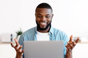 Web Conference. Cheerful Millennial African American Man Having Call On Laptop, Smiling Black Guy Sitting At Desk With Computer, Taking And Gesturing At Camera, Enjoying Online Communication photo