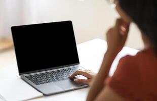 Over shoulder shot of unrecognizable businesswoman working on laptop with black empty screen, hands typing on computer keyboard while working in office, cropped image photo