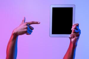 Hands Of African Male Holding And Pointing At Digital Tablet With Black Blank Screen Over Purple Neon Background, Unrecognizable Man Demonstrating Free Copy Space For App Or Website Design, Mockup photo