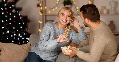 Joyful man and woman spending time at home during winter holidays, eating popcorn and laughing, copy space photo