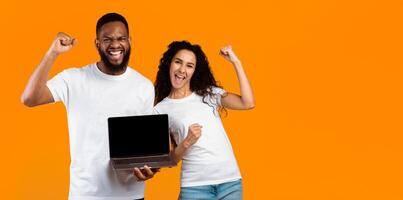 Multiracial Couple Showing Laptop Blank Screen Gesturing Yes Standing Over Yellow Studio Background. Man And Woman Recommending Website Showing Computer Monitor. Mockup, Panorama With Copy Space photo