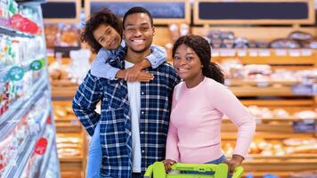 Portrait of happy black family posing together at grocery store. African American parents with cute daughter looking at camera and smiling at shopping mall. Satisfied customers at supermarket photo