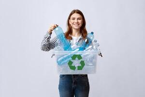 Waste For Recycling. Cheerful Young Woman Carrying Container Box With Empty Plastic Bottles, Positive Millennial Lady Sorting Garbage, Enjoying Zero Waste Living, Standing On Grey Studio Background photo