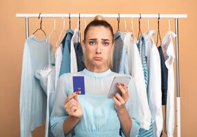 Debt, Failed Transaction, Lack Of Money. Portrait of sad upset female customer holding credit card with limit and using mobile phone, having problems with purchase in store and online payment photo