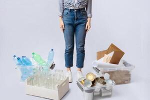 Cropped Image Of Woman Standing Next To Boxes With Different Sorted Garbage, Unrecognizable Lady Sorting Waste For Reuse And Recycling, Posing Over Light Background In Studio, Copy Space photo