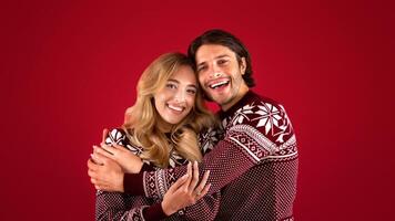 It's Christmas. Affectionate young couple in winter clothes hugging on red background photo