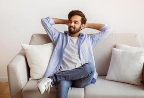 Weekend At Home. Relaxed Arab Guy Leaning Back On Couch With Hands Behind Head, Cheerful Middle Eastern Man Resting On Comfortable Sofa In Cozy Living Room , Enjoying Spending Day Off, Copy Space photo
