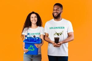 Care For Nature. Two Happy Volunteers Holding Plant And Used Plastic Bottles Smiling Each Other Posing Standing Over Yellow Studio Background. Don't Litter. Ecology And Protection Of Environment photo