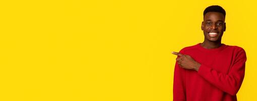 Cool Offer. Positive african american guy pointing aside at copy space on yellow background, cheerful black man showing free place for your design or advertisement and smiling at camera, panorama photo