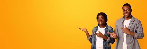 Check This. Happy Smiling Black Couple Pointing Aside At Copy Space, Positive African American Lovers Showing Free Place, Recommending Something While Standing Isolated On Yellow Background, Panorama photo