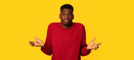 I Don't Know. Doubtful African American Guy Shrugging Shoulders And Spreading Arms, Unsure Black Guy Can't Decide What To Do, Standing Isolated Over Yellow Studio Background, Copy Space photo