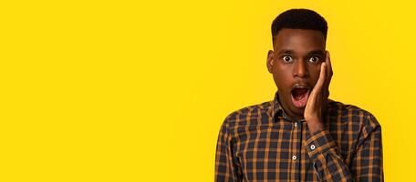 Unbelievable. Portraif Of Shocked Young Black Man Touching Face With Excitement, Amazed African American Guy Standing With Opened Mouth And Looking At Camera, Isolated On Yellow Background, Copy Space photo