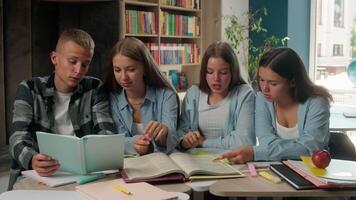 Four teenagers classmates reading book together preparing for exams showing ok gesture looking at camera smiling doing homework talking discuss good alright education studying pupils in school library video