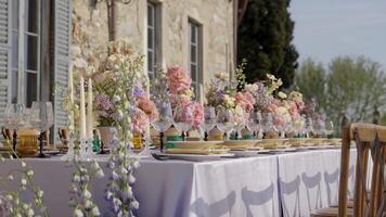 Elegant wedding table setting with floral centerpieces in front of a stone house. Action video