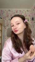 applying foundation with a pink sponge to a beautiful teenage face of a young girl doing makeup step by step in a pink room, a brunette with curls is getting ready for an event video