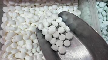 pile of assorted white round tablets, elongated capsules, and translucent softgel pills scattered across a dark wooden surface, with side lighting accentuating the contours, stamped score lines, video