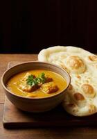 Delicious butter chicken curry with naan bread on a wooden table photo
