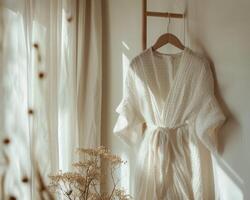 A robe hanging on a wooden hanger in front of a window photo