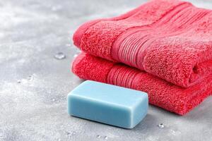 Soft red towels stacked neatly beside a blue soap bar on a textured gray surface, creating a serene and inviting bathroom atmosphere for relaxation and self-care photo