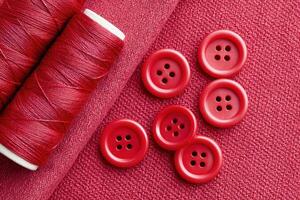 Red buttons and thread spools lying on red fabric photo