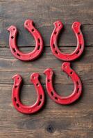 Four red horseshoes arranged on a rustic wooden surface, showcasing their unique shapes and textures, symbolizing good luck and tradition in equestrian culture photo