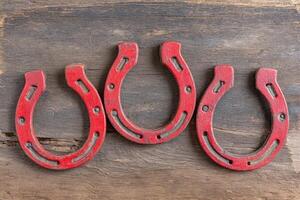 Three red horseshoes arranged on a rustic wooden surface, showcasing their unique shapes and textures, symbolizing luck and tradition in equestrian culture photo