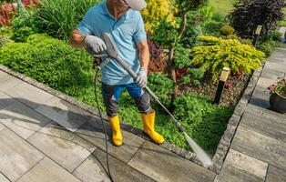 Man Pressure Washing a Stone Pathway in a Vibrant Garden During Sunny Weather photo