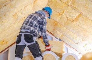 Construction Worker Installing Insulation in Residential Attic on a Bright Sunny Day photo