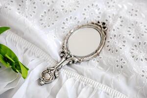 Decorative vintage hand mirror placed on white embroidered fabric with green leaves photo