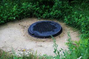 Manhole cover surrounded by grass and dirt in a natural setting on a cloudy day photo