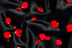 Bright red rose petals scattered on a smooth black fabric creating a striking contrast photo