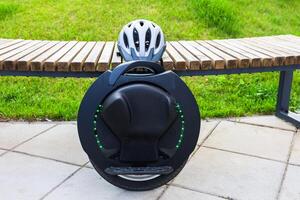 Modern unicycle parked on a wooden bench in a park with green grass and a helmet resting nearby photo