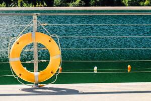Lifesaving ring mounted on a dock by a tranquil lake surrounded by greenery photo
