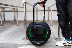 Modern electric unicycle being carried by a person in urban environment near railings photo