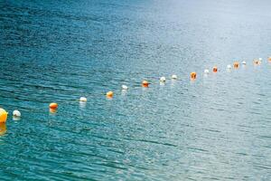 Bright buoy markers floating along a tranquil lake during a sunny day photo