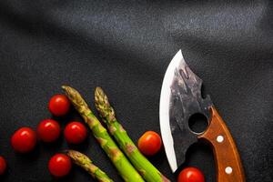 Fresh vegetables and a unique knife are displayed on a dark background for meal preparation photo