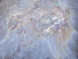 A multi-colored gasoline stain on the road on the melted snow. photo