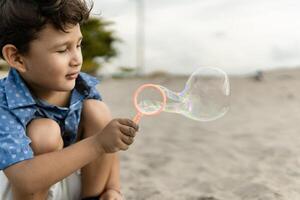 Little boy making soap bubbles on the beach with a bubble blower toy photo