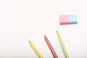 Three colored pencils and an eraser on white paper. photo