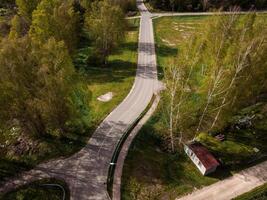 An aerial view shows intersecting roads, open grassy areas, sparse trees, and a small red roofed structure with white walls in the lower right corner. photo