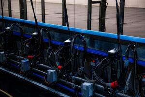 Row of milking machine units with pipes, hoses, and control boxes on a metallic structure. Wet floor indicates recent cleaning or use in the facility. photo